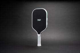 TMP Stealth Pickleball Paddle from Tickle My Pickle, angled view showing the TMP-branded black face with white frame, on a black gradient background