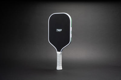 TMP Stealth Pickleball Paddle from Tickle My Pickle, angled view showing the TMP-branded black face with white frame, on a black gradient background