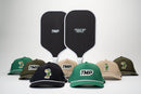 Two TMP Stealth Pickleball Paddles standing side by side, showing the TMP face and Tickle My Pickle face, with the TMP Performance Pickleball Hat lineup arranged at the base